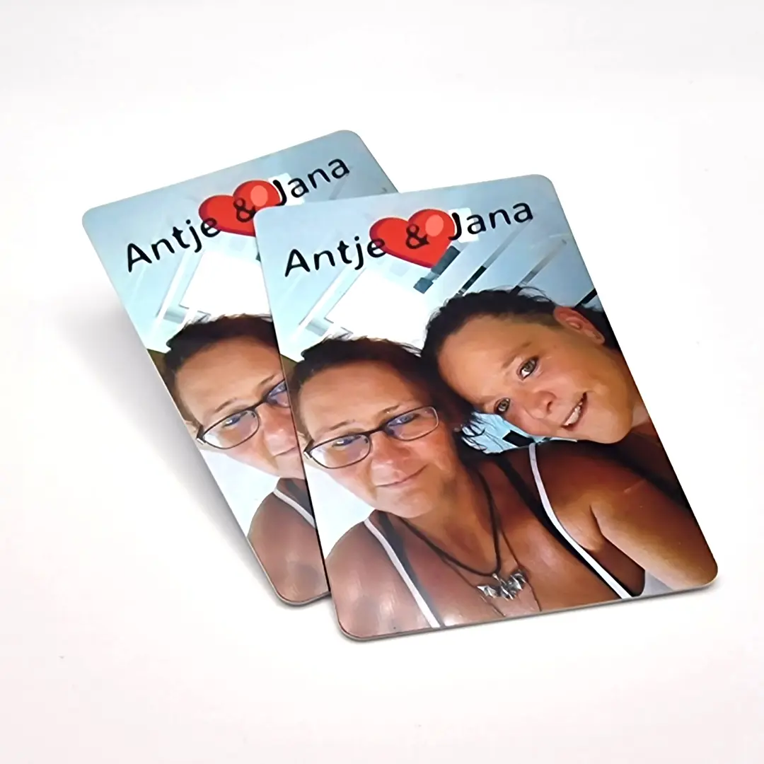 Foto zweier hochformatig bedruckter PVC-Plastikkarten auf weißem Hintergrund. Die Karten zeigen ein Farbfoto zweier lächelnder Frauen mit Brille und den Schriftzug „Antje & Jana“ mit einem roten Herz-Symbol am oberen Rand.