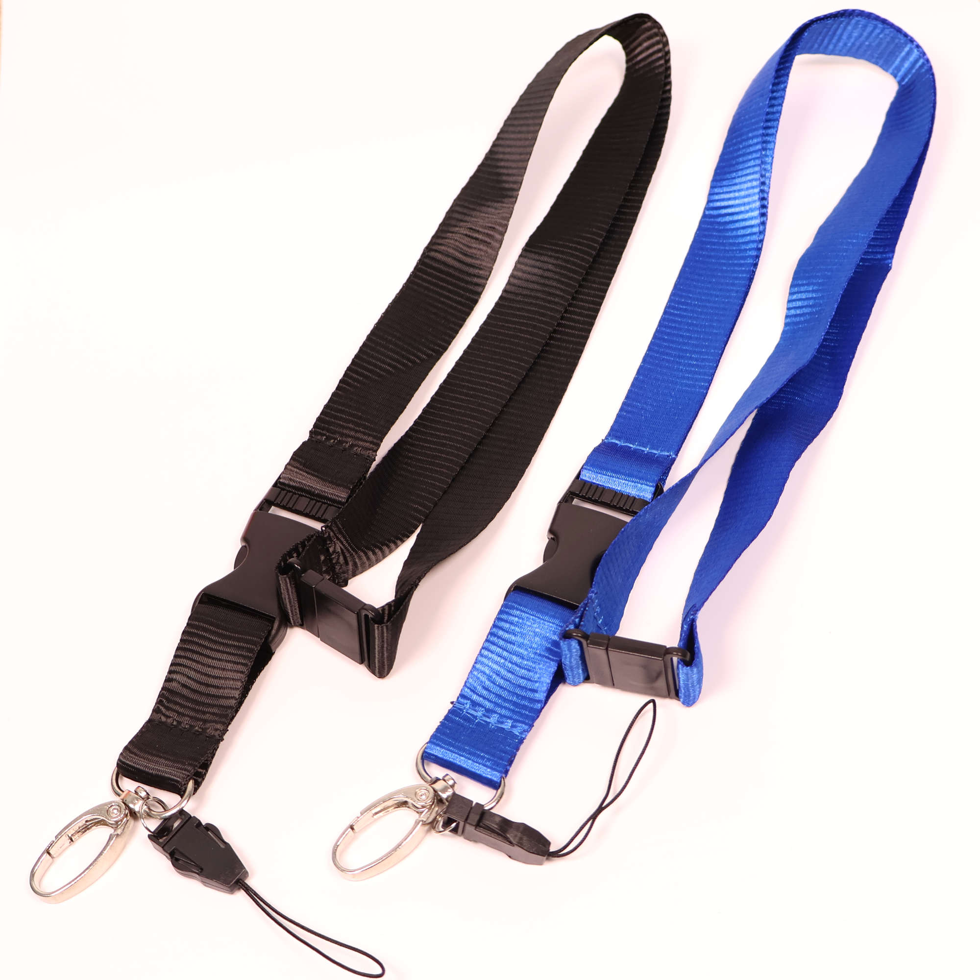 Zwei flache Schlüsselbänder in Schwarz und Blau nebeneinander auf weissem Grund. Beide Lanyards verfügen über eine abnehmbare Steckschnalle, einen Sicherheitsverschluss sowie einen Metallkarabiner und eine zusätzliche dünne Kordelschlaufe.