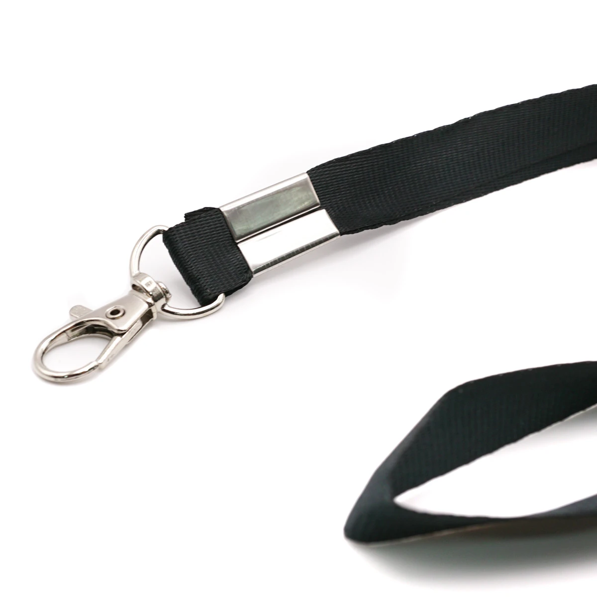 Nahaufnahme des schwarzen Flachband-Schlüsselbands mit silberfarbenem Metallkarabiner und Klemmschnalle auf weissem Hintergrund. Im Vordergrund rechts ist ein Teil der Bandschlaufe unscharf abgebildet.